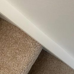 Close-up of a carpeted staircase with a white wall above, viewed from an angle.