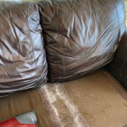 Brown leather couch with pet hair on the seat and a handheld vacuum cleaner resting on the armrest.
