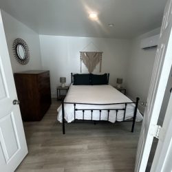 Small bedroom with a double bed, two nightstands, dresser, wall art, and an air conditioner on the right wall.