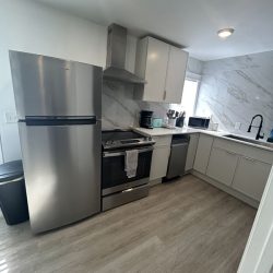 Modern kitchen with stainless steel appliances, white cabinets, marble backsplash, and light wood flooring.
