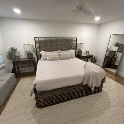Bedroom with wicker bed frame, neutral bedding, two lamps on side tables, and a large mirror against the wall.