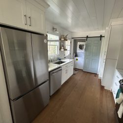 Narrow kitchen with stainless steel appliances, white cabinets, wood floor, and a blue sliding barn door at the end.