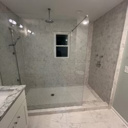 Modern bathroom with a walk-in shower, marble tiles, a glass partition, and a window on the shower wall.