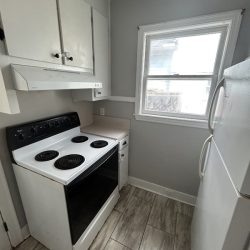Small kitchen with electric stove, refrigerator, white cabinets, tile floor, and a window letting in natural light.
