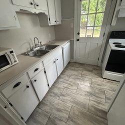 Small kitchen with white cabinets, stainless sink, microwave, stove, and a door leading outside; gray tiled floor.